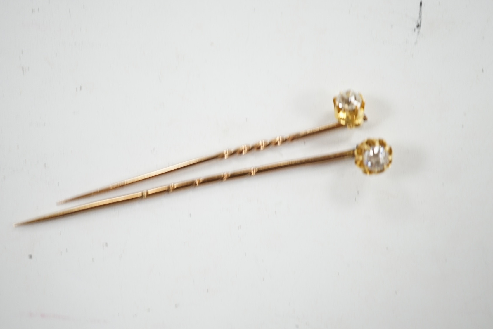 Two early 20th century yellow metal and solitaire diamond set stick pins, 65mm and a dress stud. Condition - fair to good